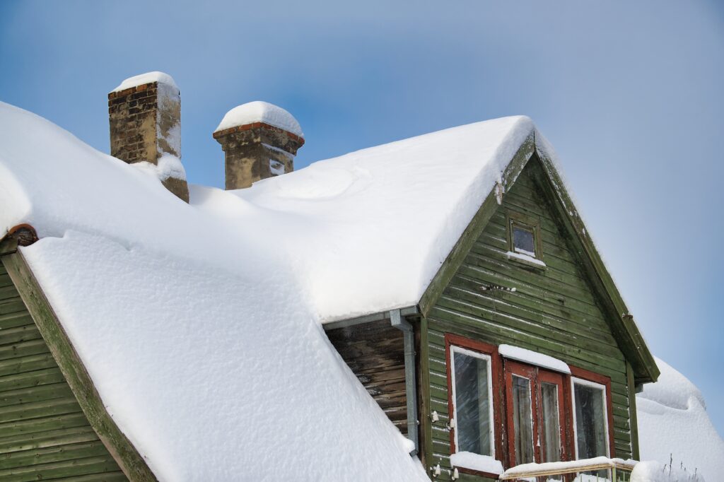 snow thickly laying on a wooden house with green paint 