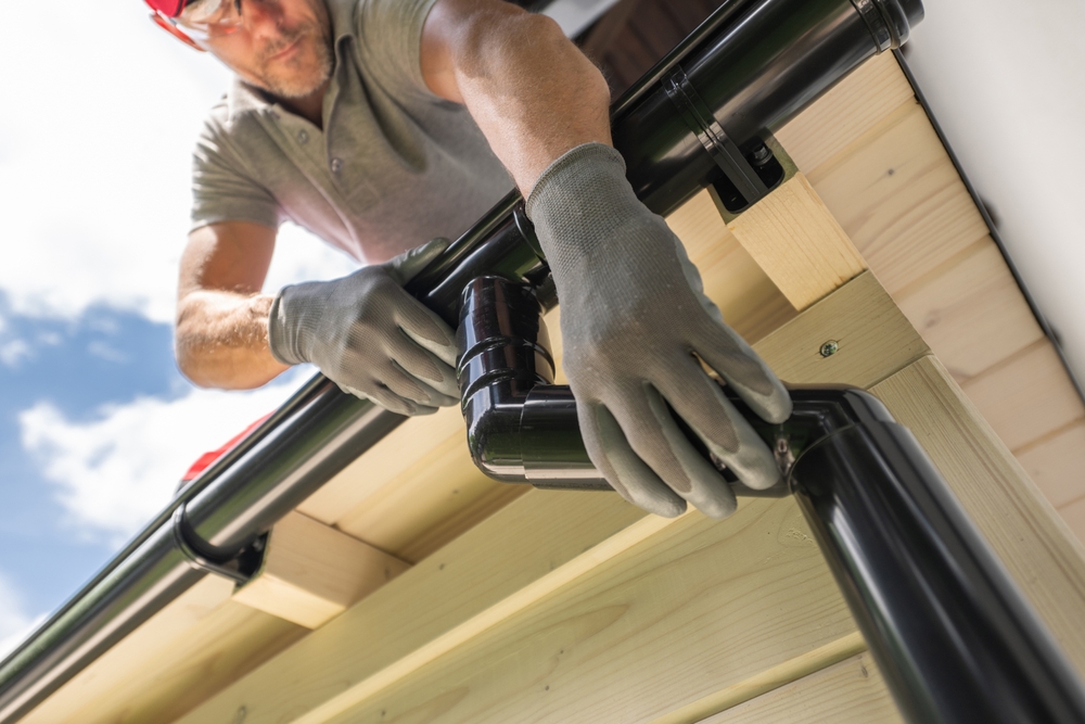 man installing gutter replacements onto a wooden house 